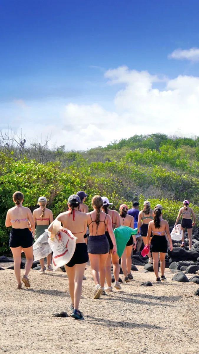 Group of teenage volunteers completing a beach cleanup session in Galapagos, carrying sacks of trash to protect the marine ecosystem.