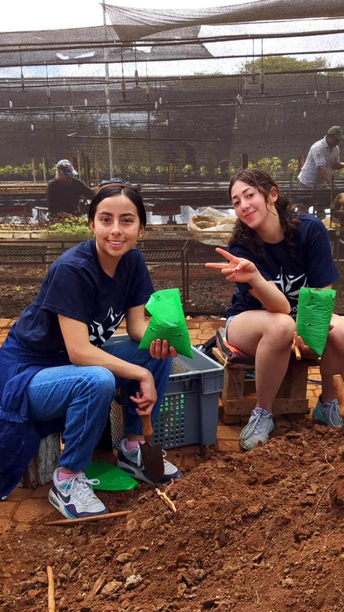 Two teenage volunteers working in a Galapagos nursery (greenhouse), holding bags of endemic plants ready for reforestation.