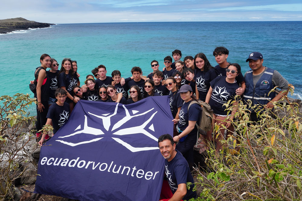 Group of Teen Camp participants in the Galapagos, holding a flag in front of the sea during an excursion.