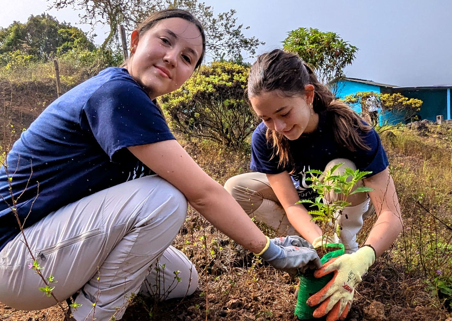 Two smiling teenage volunteers planting an endemic plant in Galapagos. The reforestation work helps to restore the natural habitat.