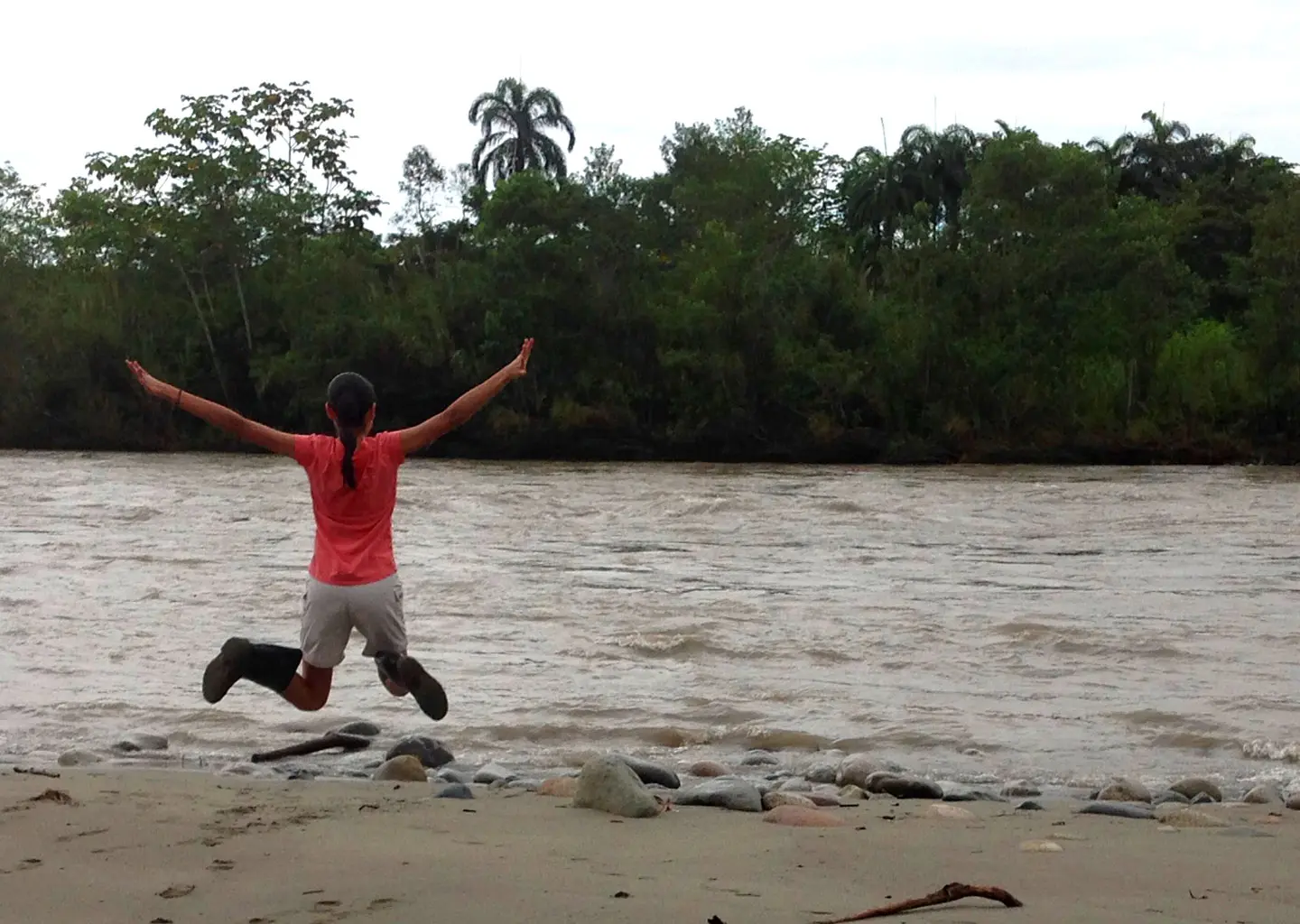 Teen participant jumping with excitement by the river during Amazon Teen Camp adventure in Ecuador rainforest